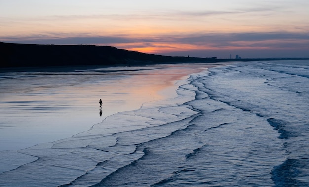 Ciel coucher de soleil avec nuages sur la plage de sable de la mer avec vague océanique le soir Paysage d'été au bord de la mer avec ciel coloré en OrangePinkPurpleBlueBelle réflexion horizontale de la lumière du soleil sur la plage de sable