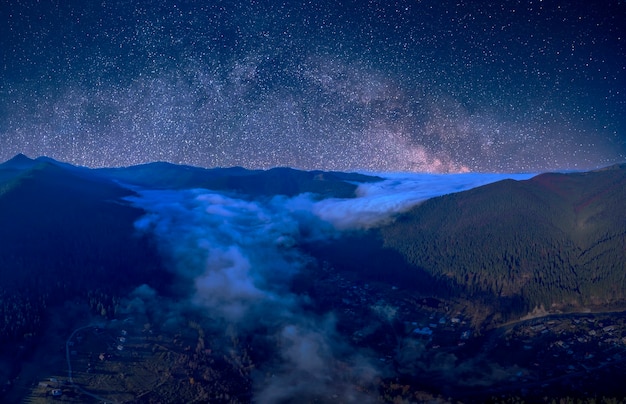 Ciel étoilé au-dessus des montagnes boisées. Le brouillard se répand dans les intermontagnes. Magnifique paysage de montagne de nuit.