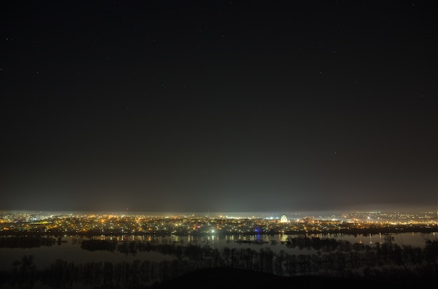 Ciel étoilé au-dessus de la ville et de la rivière pendant les crues printanières. Paysage avec une longue exposition.