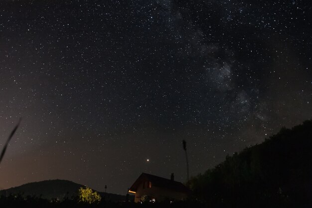 Ciel étoilé de nuit avec le toit de la maison au premier plan, camping à la montagne