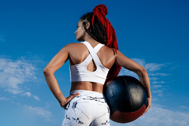 Ciel de fond. De derrière. Femme athlétique avec ballon médical. Force et motivation Photo de femme sportive en vêtements de sport à la mode