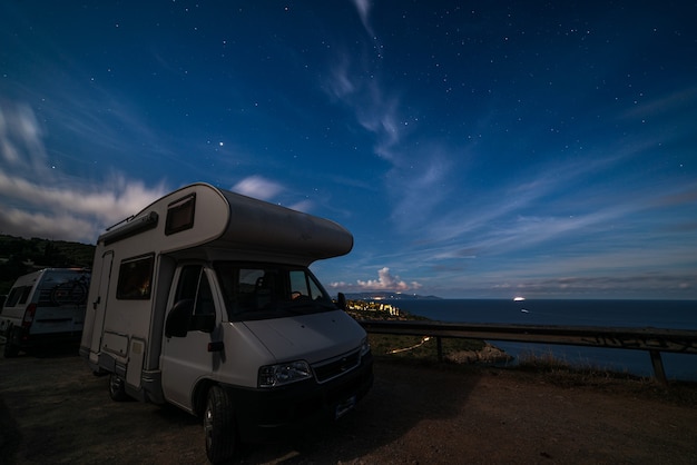 Ciel nocturne à la péninsule de Monte Argentario, Toscane, Italie. Étoiles au-dessus du camping-car illuminé par la lumière de la lune. L'île de Giglio en arrière-plan.