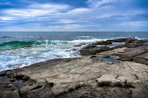 Ciel nuageux au-dessus de la mer vagues turquoise se brisant sur les rochers