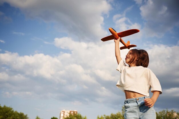 Ciel nuageux Une petite fille heureuse joue avec un avion jouet à l'extérieur