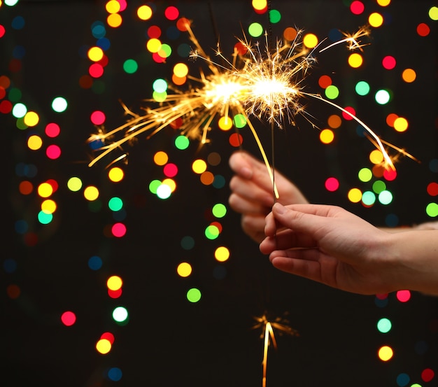 Cierge magique dans la main de la femme sur les lumières colorées de bokeh