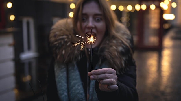 Cierges magiques brûlants dans les mains d'une jeune femme dans l'obscurité