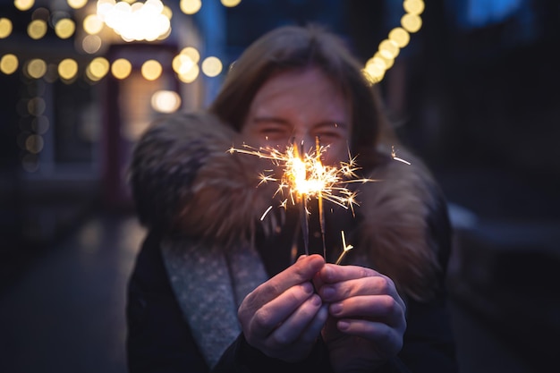 Cierges magiques brûlants dans les mains d'une jeune femme dans l'obscurité