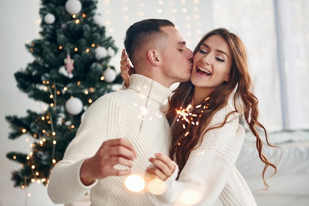 Avec des cierges magiques dans les mains Un jeune couple romantique célèbre le Nouvel An ensemble à l'intérieur