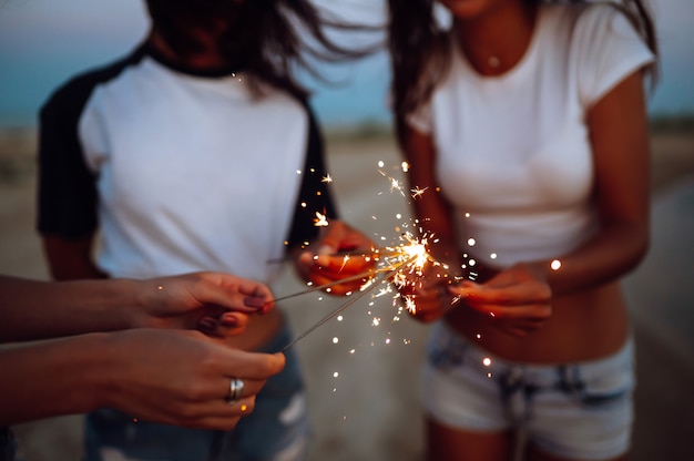 Les cierges magiques entre les mains des jeunes filles sur la plage. Trois filles profitant d'une fête sur la plage avec des cierges magiques. Concept de vacances d'été, vacances, détente et style de vie.