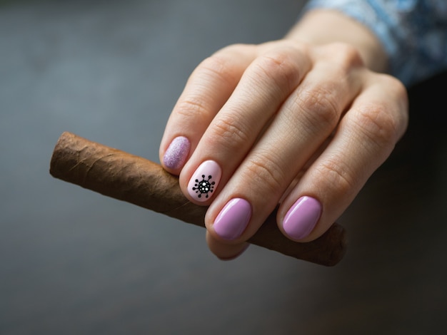 Cigare à la main de la femme, photo sur table grise. Manucure créative avec virus peint sur les ongles, flou, gros plan.