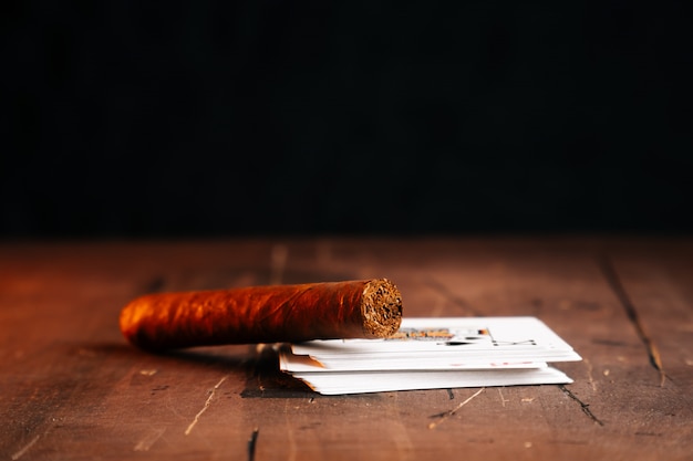 Un cigare sur la table à côté d'un jeu de cartes sur une table marron foncé