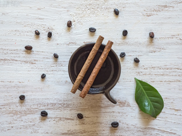 Cigares sur une tasse de café noir avec des grains de café.