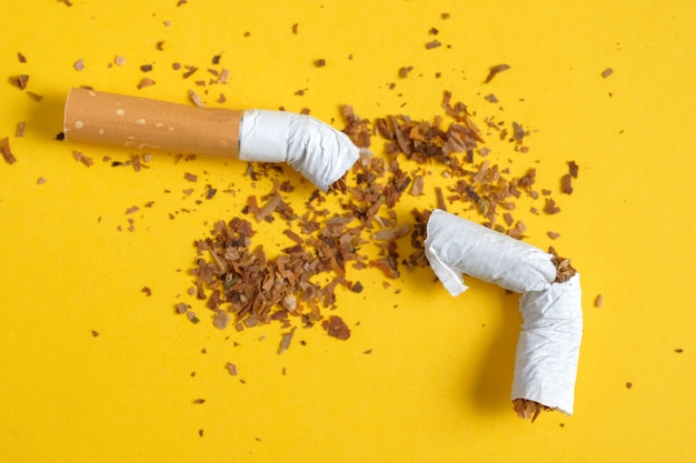 Cigarette cassée en deux avec une rangée de tabac dispersé sur jaune