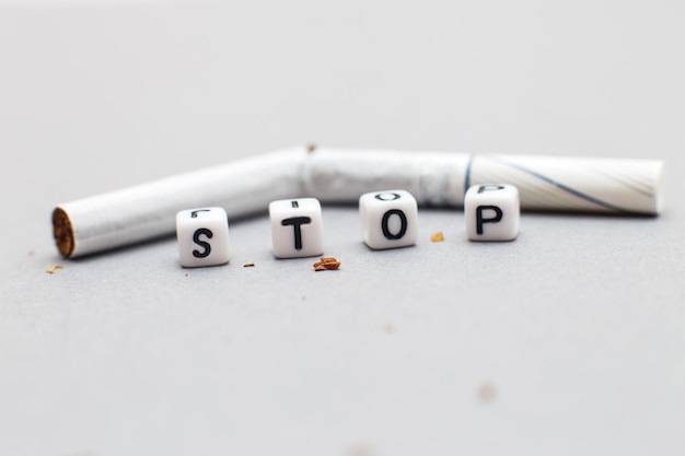 Cigarette cassée avec le mot stop sur fond gris à proximité. arrêter de fumer