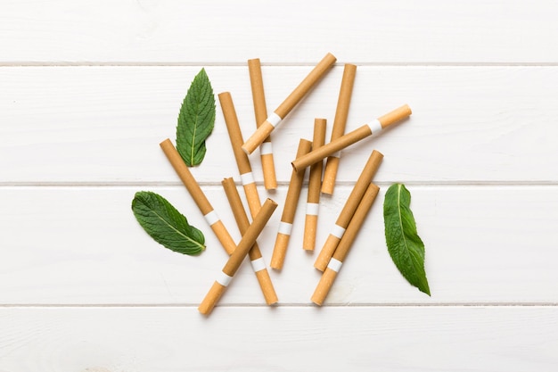 Cigarettes au menthol et feuilles de menthe fraîche sur fond coloré Beaucoup de cigarettes empilées vue de dessus mise à plat