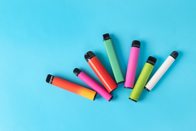 cigarettes électroniques jetables colorées sur un fond bleu Le concept de tabagisme moderne