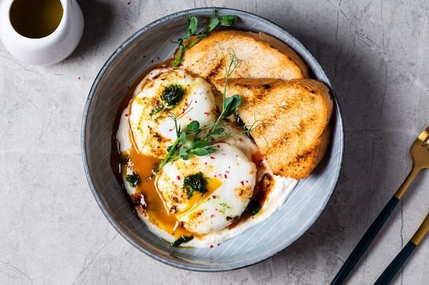 Cilbir ou oeufs turcs. plat servi comme mezze : œufs pochés nappés de yaourt grec aux herbes, puis arrosés d'huile d'olive piquante au paprika épicé. Petit-déjeuner turc dans un bol gris sur fond de marbre