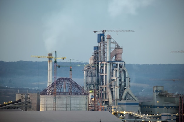 Cimenterie avec structure d'usine élevée et grues à tour dans la zone de production industrielle Fabriquer un concept mondial d'industrie et de pollution de l'air