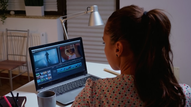 Cinéaste éditant un film à l'aide d'un logiciel moderne de post-production. Vidéaste travaillant sur un montage de film audio sur un ordinateur portable professionnel assis sur un bureau dans une cuisine moderne à minuit