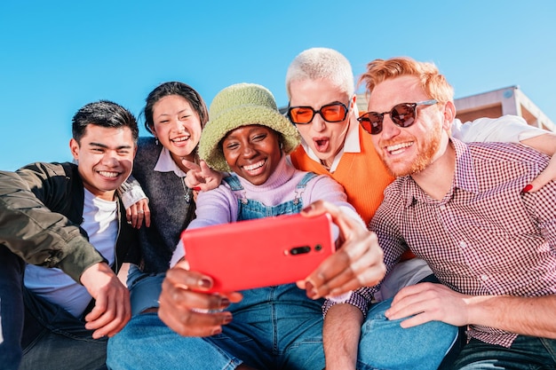 Cinq amis multiraciaux prenant un selfie ensemble à l'extérieur sous un ciel bleu