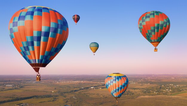 Cinq ballons colorés dans les airs au-dessus des plaines.