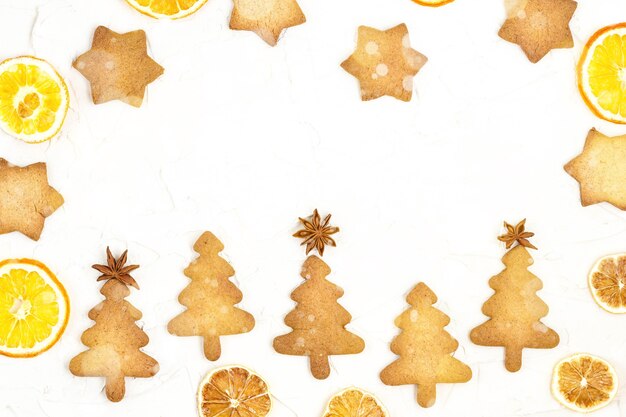 Cinq biscuits d'arbre de Noël avec des décorations en étoile et de l'orange sèche sur fond blanc avec fond. Bokeh tonique et neige