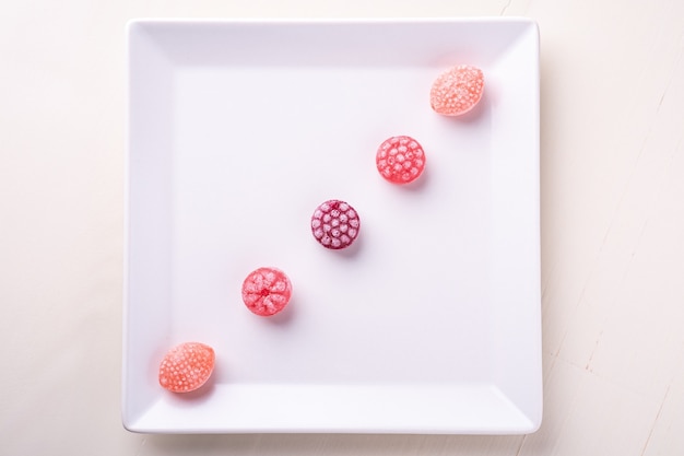 Cinq bonbons de cannes de bonbon sous forme de baies juteuses sur une plaque blanche sur fond blanc isolé, vue du dessus