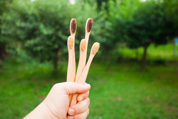 Cinq brosses à dents en bambou dans une main sur des motifs naturels défocalisés. Hygiène et mode de vie respectueux de l'environnement
