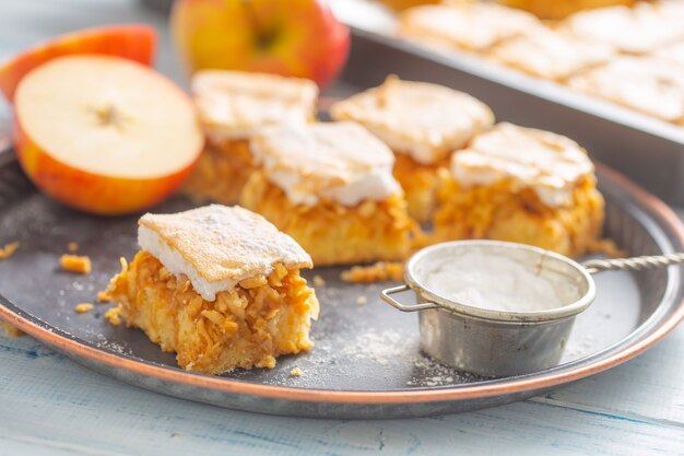 Cinq cubes de pomme avec une garniture à la crème, un tamis à sucre et une demi-pomme à côté.