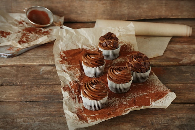 Cinq cupcakes au chocolat sur papier boulanger sur fond de bois