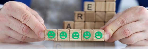 Cinq émoticônes souriantes vertes sur des cubes dans les mains d'un homme d'affaires prospère