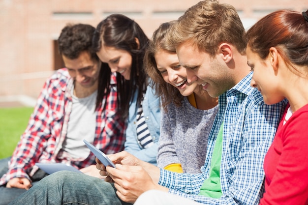 Cinq étudiants souriants assis sur l&#39;herbe avec une tablette