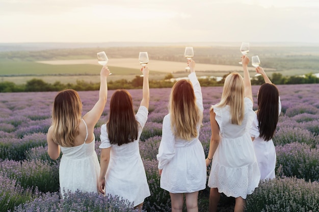 Cinq femmes en robes blanches brandissent des verres de vin dans un champ de lavande