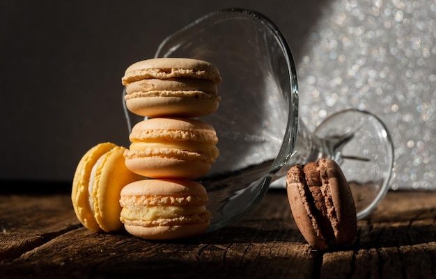 Cinq macarons crémeux bruns et jaunes près d'un verre sur le fond en bois