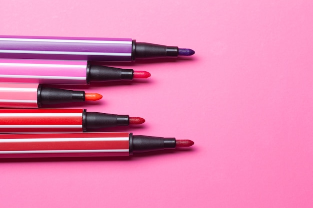 Cinq marqueurs ouverts ou stylos de couleur rose, violet, rose se trouvent comme des marches sur un rose