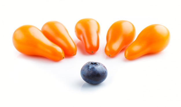 Cinq petites tomates raisins orange mûres et une seule myrtille isolée sur fond blanc. vue de côté