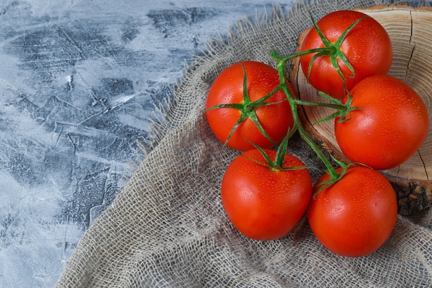 Cinq tomates reposent sur un support en bois et un chiffon en coton.