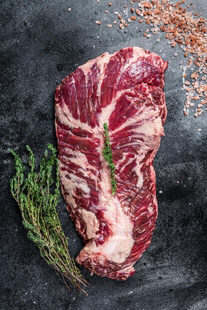 Cintre ou onglet steak de viande de boeuf cru sur table de boucher avec des herbes. Fond noir. Vue de dessus.