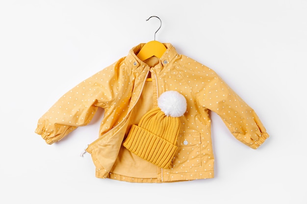 Photo cintre suspendu veste jaune avec chapeau sur fond blanc. jolie tenue d'automne pour enfants.