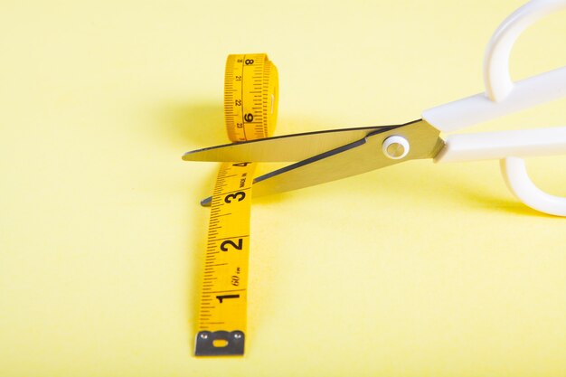 Photo les ciseaux coupent le ruban à mesurer sur fond jaune