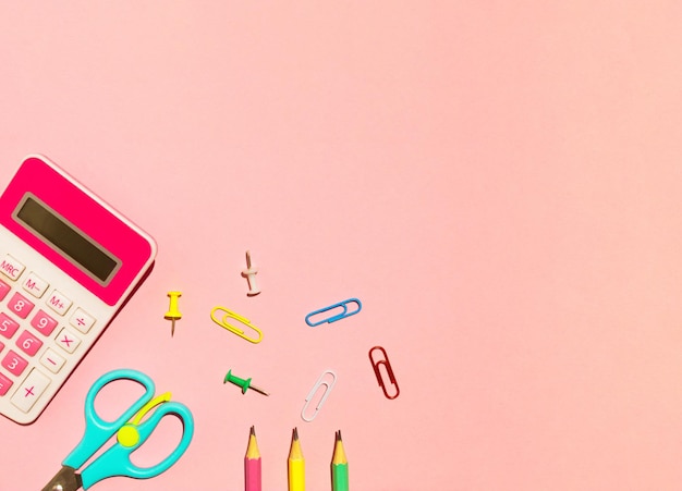 Ciseaux crayon calculatrice scolaire et trombones sur fond rose Concept de retour à l'école mise à plat