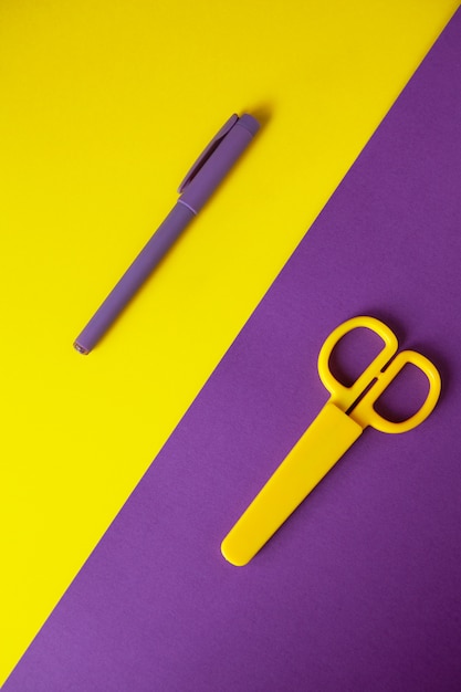 Ciseaux de papeterie pour enfants jaune sur fond violet, stylo pourpre sur fond jaune.