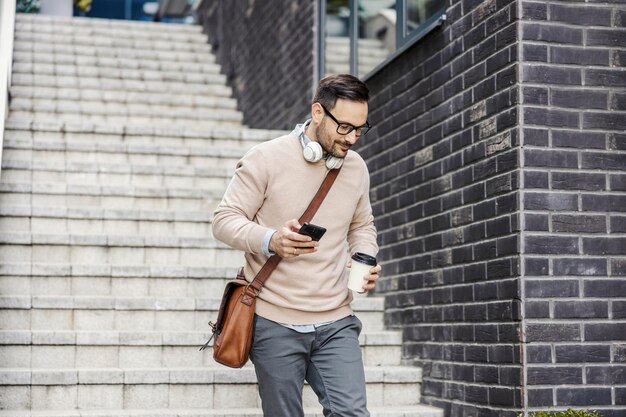 Un citadin descendant les escaliers à l'extérieur et transportant un téléphone et du café à emporter