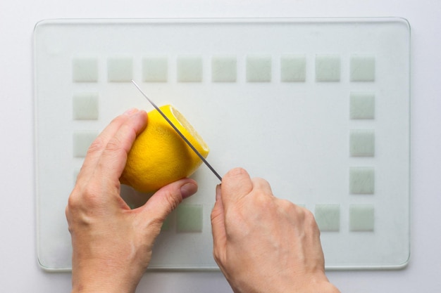 Citron coupé à la main de femme avec un couteau sur fond blanc