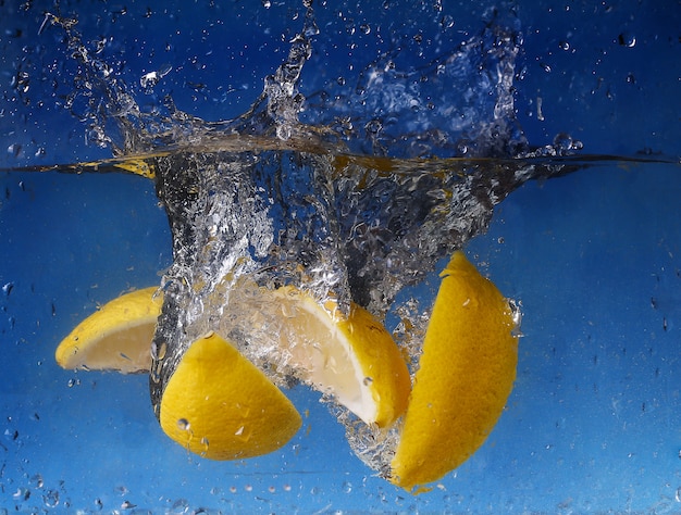 Citron entier tombé dans l'eau contre un mur bleu dégradé