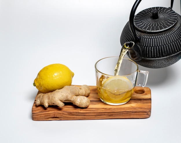 Citron, gingembre et une tasse de thé au citron sur une planche d'olive sur fond blanc