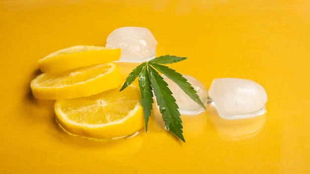 Citron rafraîchissant avec saveur de marijuana et glaçons sur fond jaune.