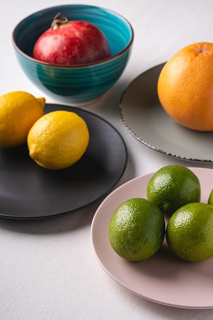 Citron vert, citron, pamplemousse et grenade dans des assiettes colorées sur blanc