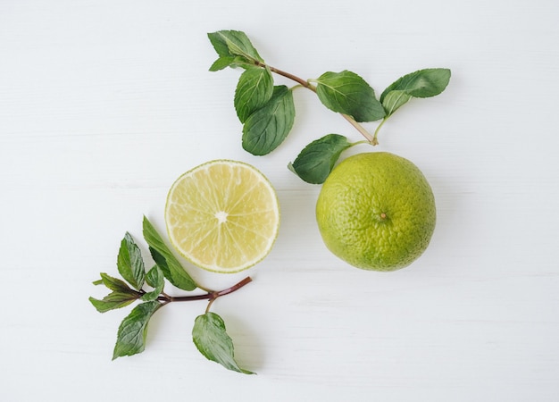 Citron vert frais et feuilles de menthe sur une surface blanche.