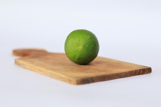 Photo un citron vert sur une planche à découper en bois est sur un fond blanc.